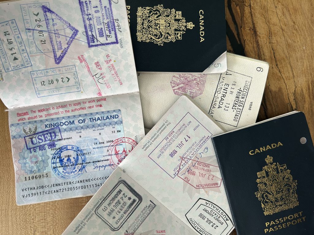 Five passports. Three are opened with stamps in them while the other two are closed, the front covers say Canada.