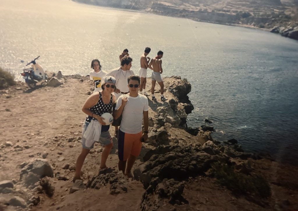 Several teenagers standing on a cliff, facing away from Red Beach in Greece.