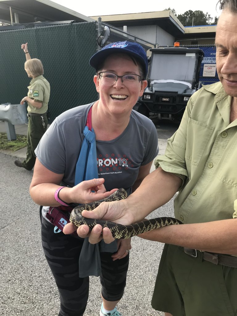 A woman in running gear during a race petting a snake.