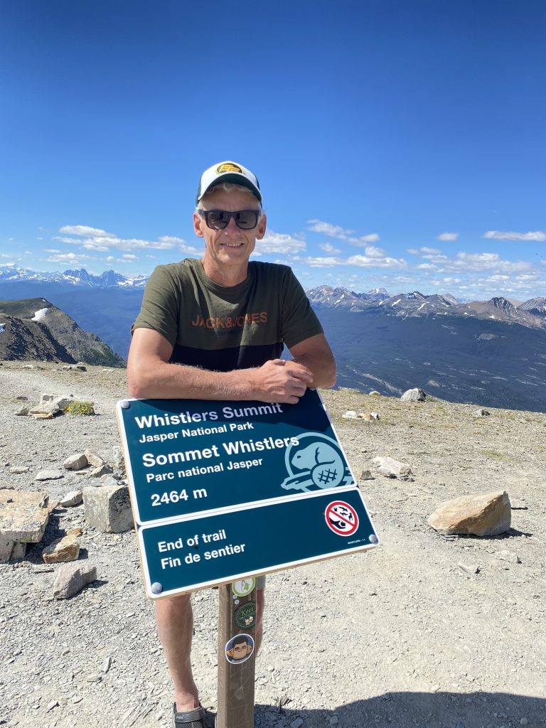 A man standing next to Whistler's Summit sign in Jasper