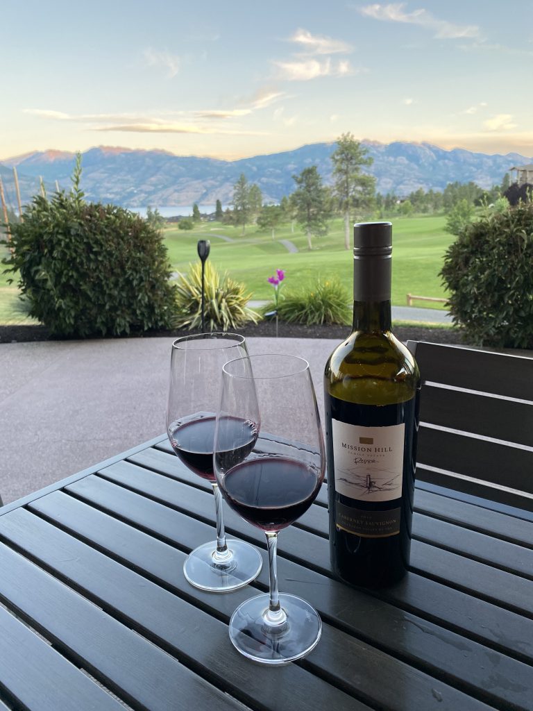 Wine and glasses on patio in front of mountains.