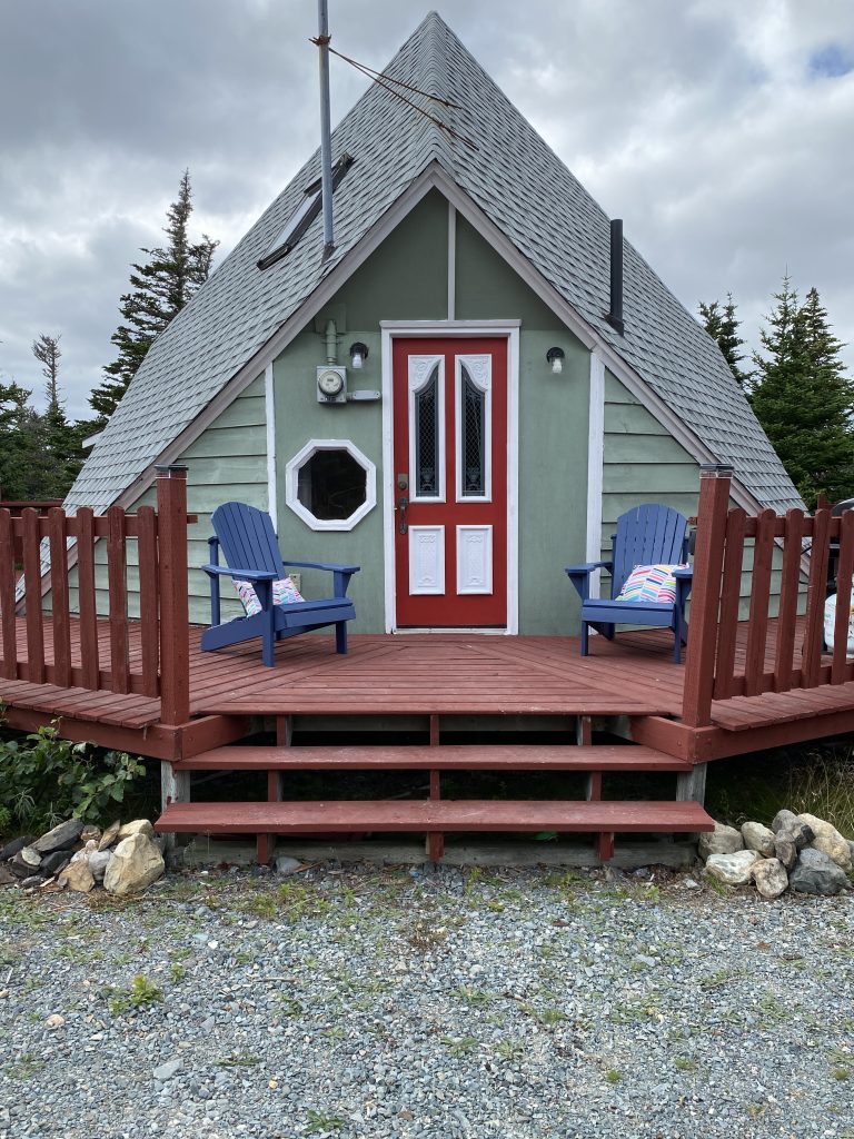 A frame cabin with red door and two blue chairs